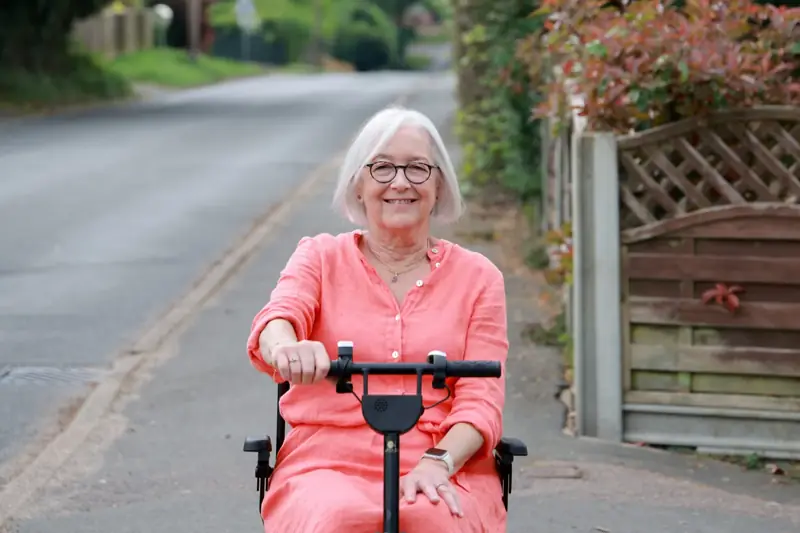 Smiling woman riding her eFOLDi mobility scooter down a quiet lane